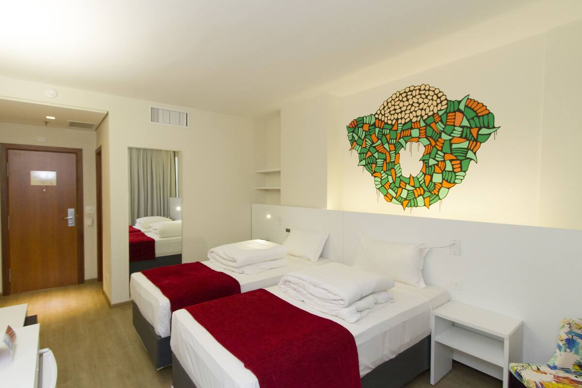 Een hotelkamer met twee bedden, een bureau en een kunstwerk aan de muur.