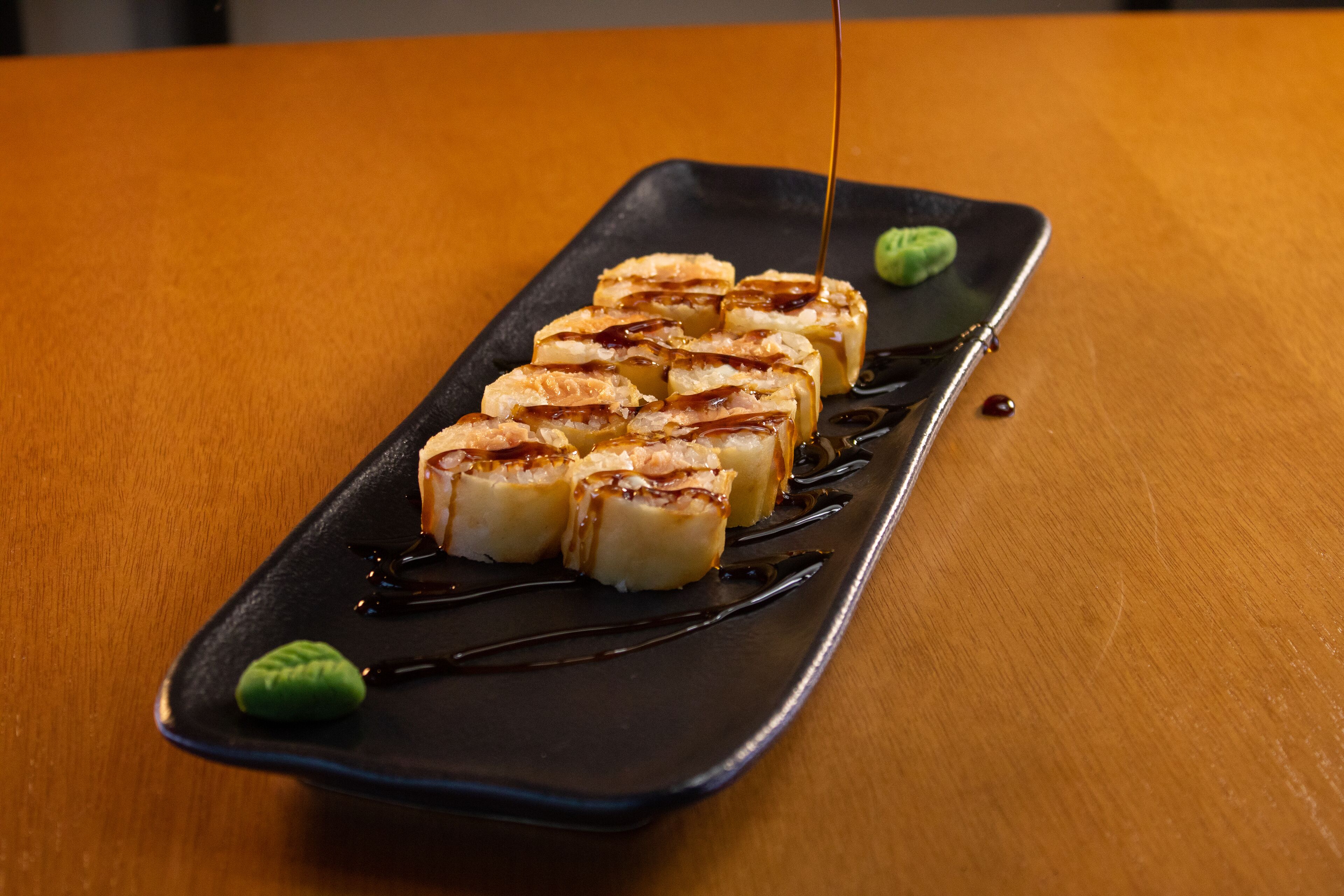 A rectangular black plate with a row of sushi pieces and green wasabi on a wooden table.
