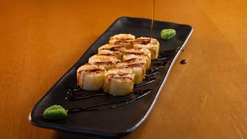 Prato preto retangular com uma fileira de peças de sushi e wasabi verde sobre uma mesa de madeira.