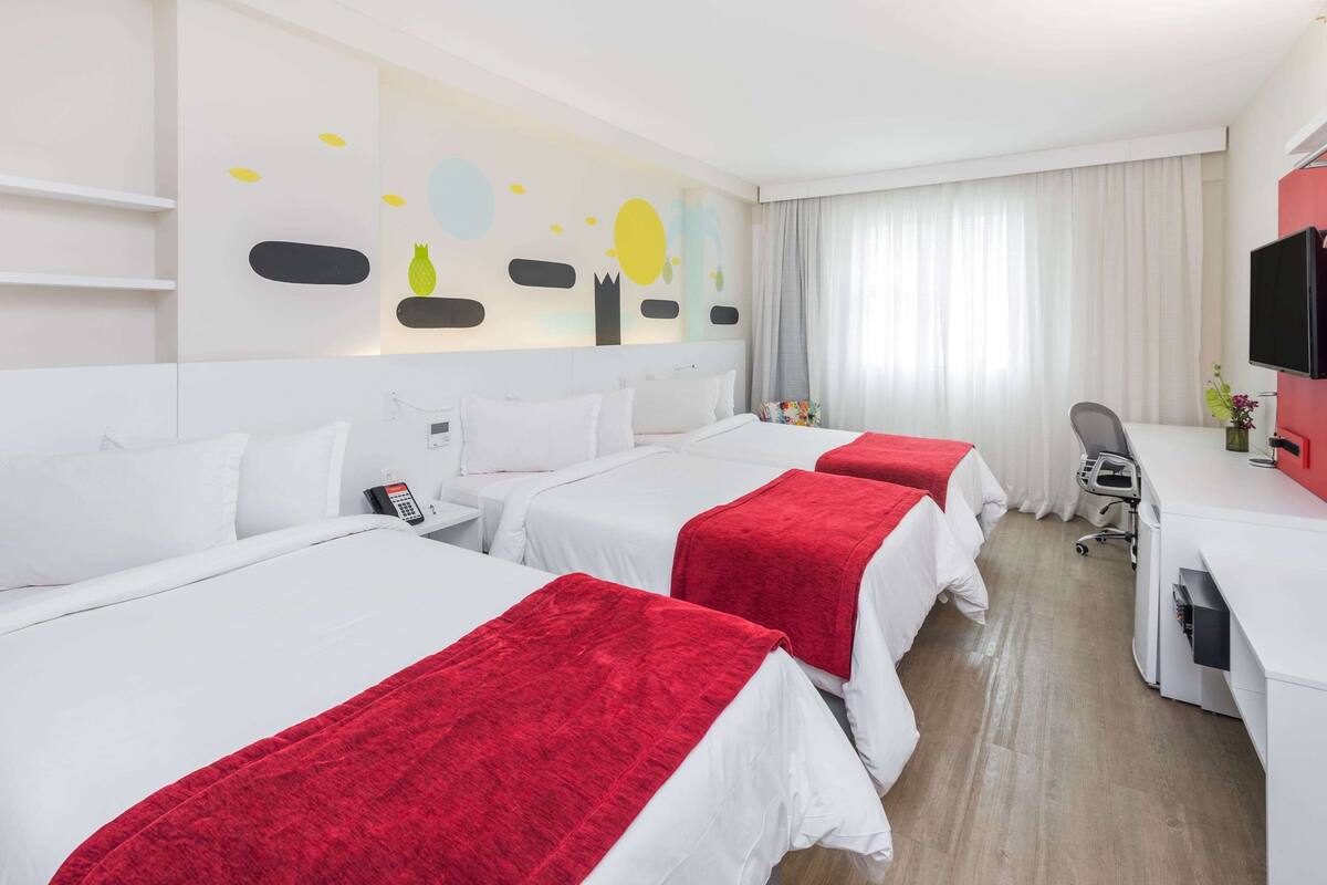 Een hotelkamer met drie bedden, een bureau, een stoel en een televisie.
