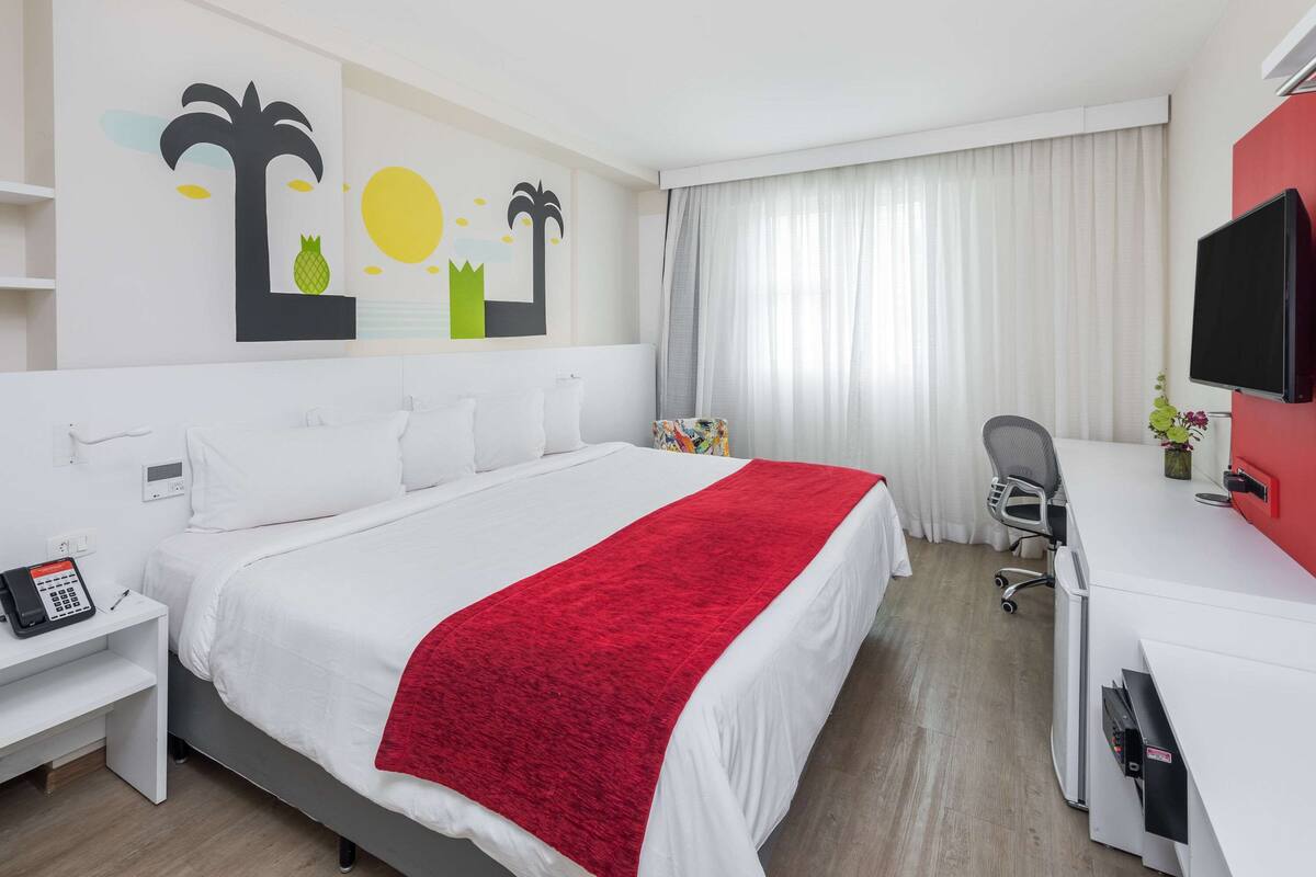 Een hotelkamer met een bed, een bureau, een stoel, een televisie en een kunstwerk aan de muur.
