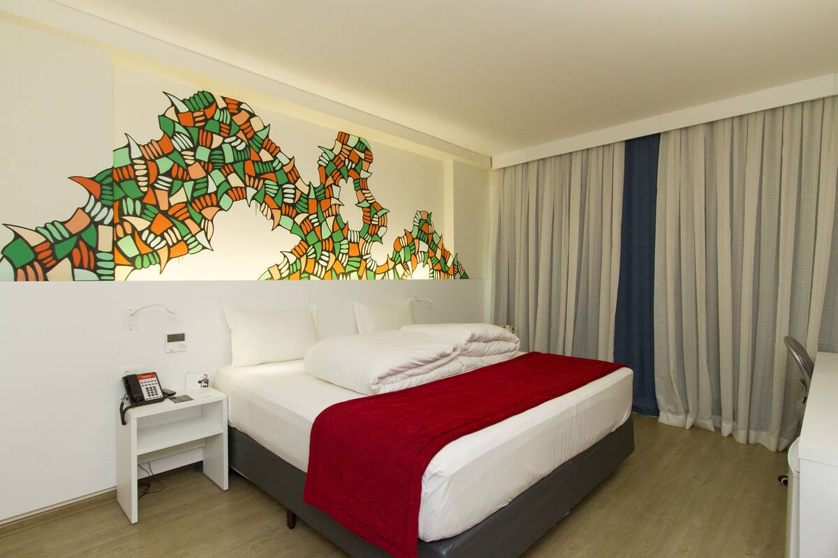 Een hotelkamer met een bed, nachtkastje, telefoon en een kunstwerk aan de muur.