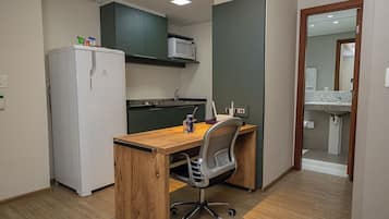 A compact kitchen with a refrigerator, microwave, and a wooden desk with a chair.