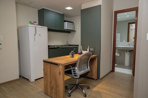 A compact kitchen with a refrigerator, microwave, and a wooden desk with a chair.