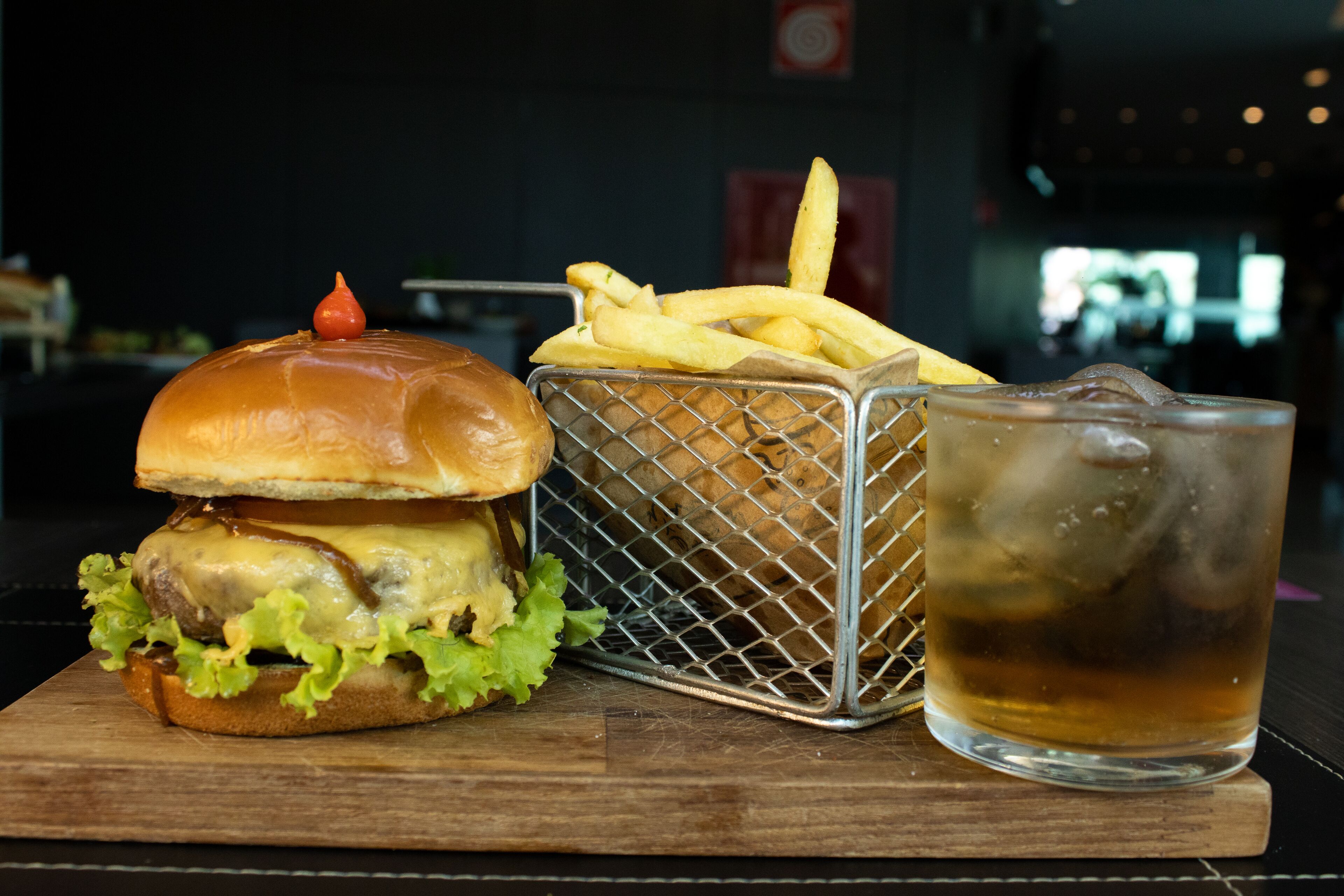 A burger, a basket of fries, and a glass of iced beverage on a wooden table.