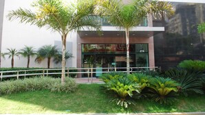 A modern building with a glass facade, a number '274' sign, and a well-maintained garden with palm trees and shrubs. - Esuites Virginia Luxemburgo BH (Belo Horizonte)