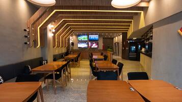 A modern restaurant with wooden tables and chairs, a bar area, and multiple screens displaying content.