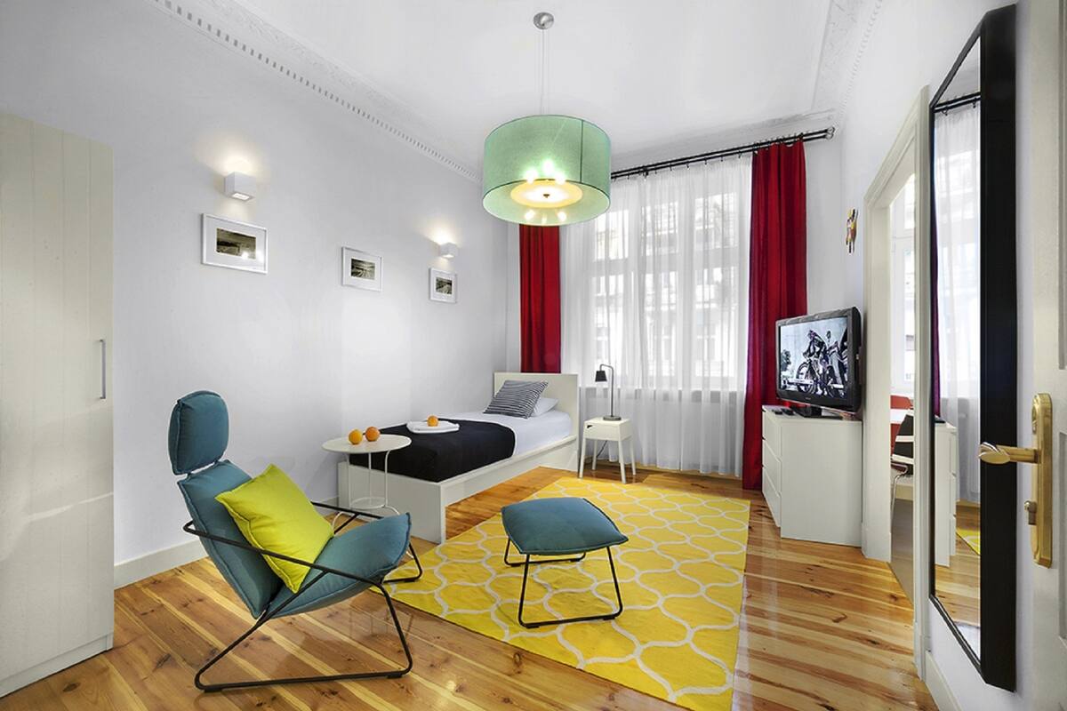 Un salon moderne comprenant un canapé, des fauteuils, une petite table, un téléviseur et une grande fenêtre avec des rideaux.