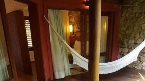 A wooden deck with a white bathtub filled with water and rose petals, a hammock, and a stone wall in the background. - Pousada dos Ponteiros (São Miguel do Gostoso)