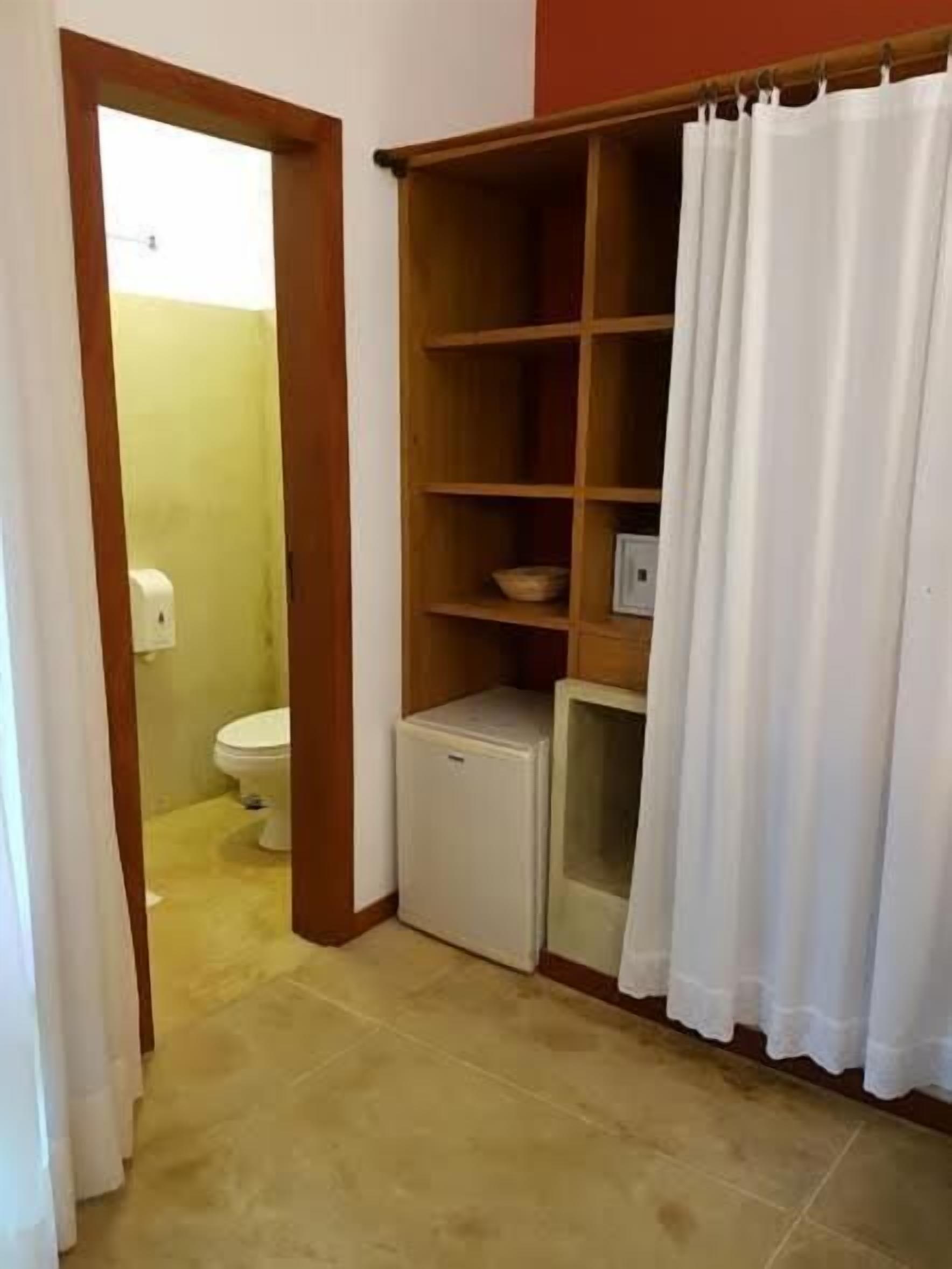 Un baño pequeño con inodoro, un refrigerador compacto y una estantería.