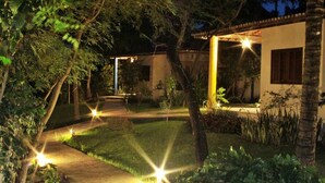 A well-lit garden pathway leading to a building with a covered patio area. - Pousada dos Ponteiros (São Miguel do Gostoso)