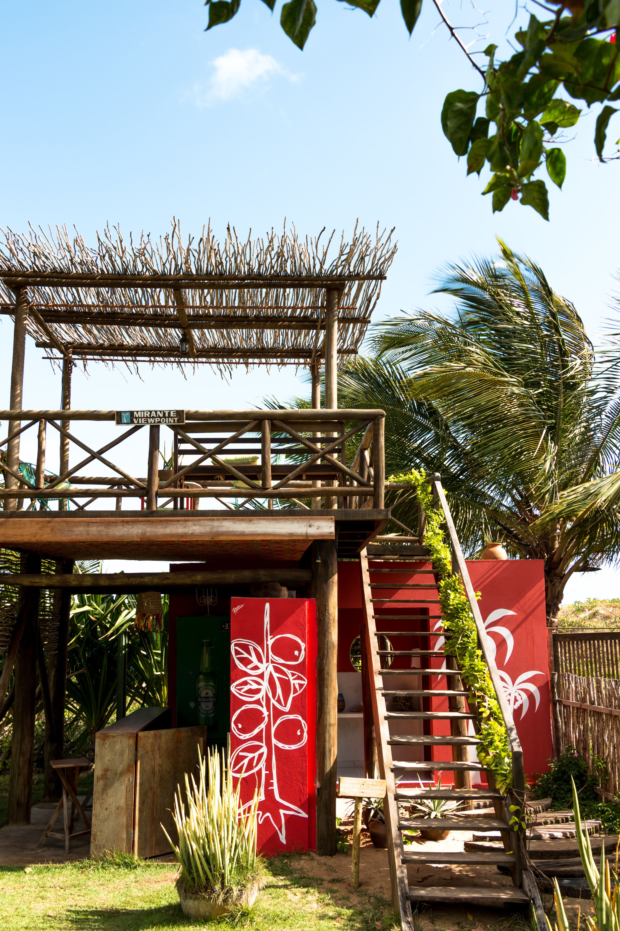 A wooden structure with a thatched roof, a red wall with white floral designs, and a staircase leading to a higher level.