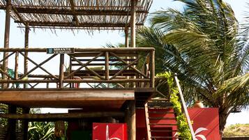 A wooden structure with a thatched roof, a red wall with white floral designs, and a staircase leading to a higher level.