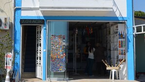 Un edificio de dos plantas con fachada azul y blanca, un balcón con barandillas y una entrada a tienda con diversos artículos expuestos en el exterior.