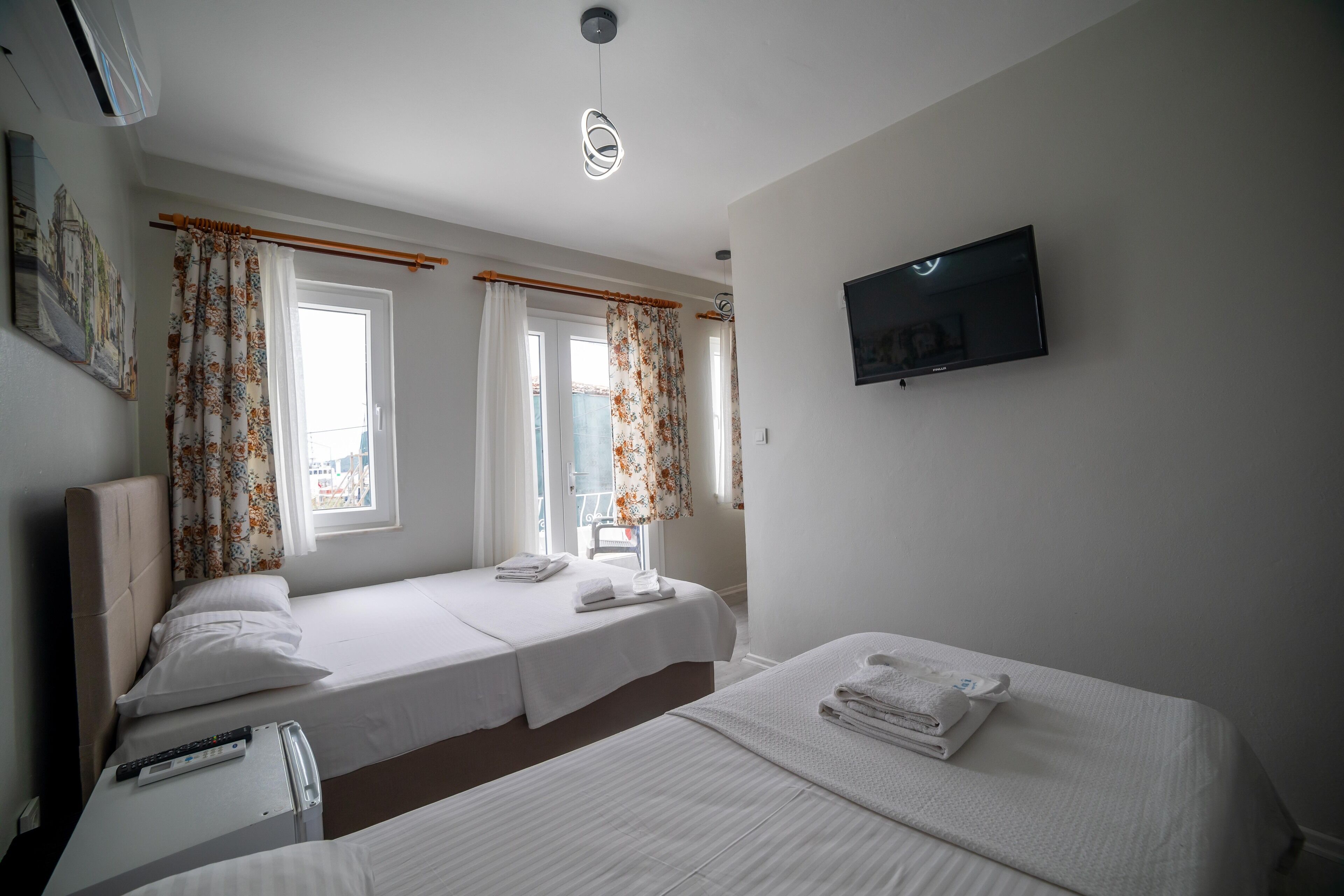 A hotel room with two beds, a flat-screen TV, and a window with curtains.