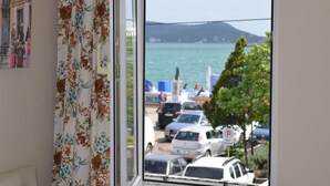 Vista a través de una ventana con cortinas florales, un área de estacionamiento con coches y una masa de agua con una montaña distante.