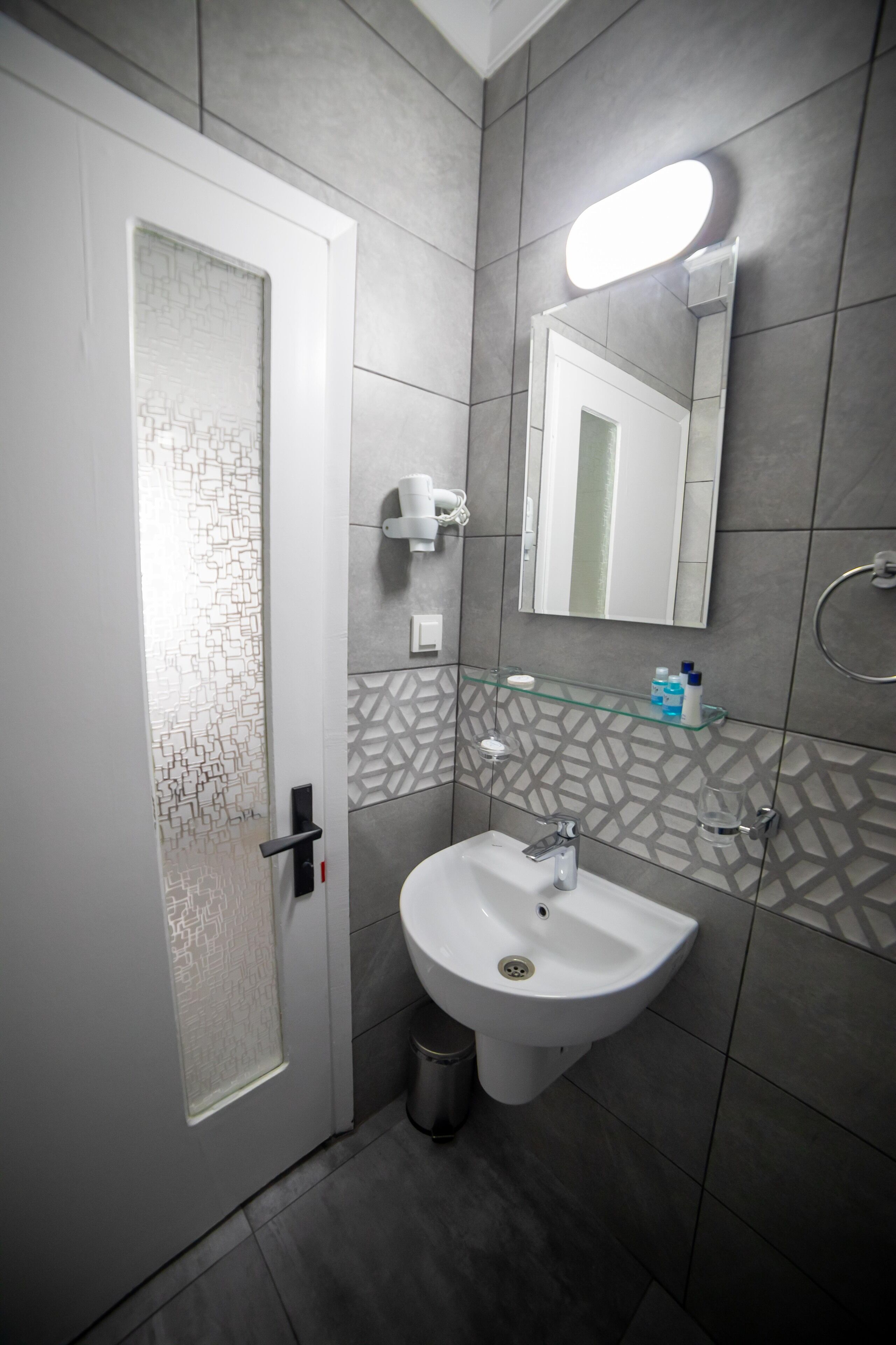 A modern bathroom with a white sink, a mirror, and a glass shelf with toiletries.