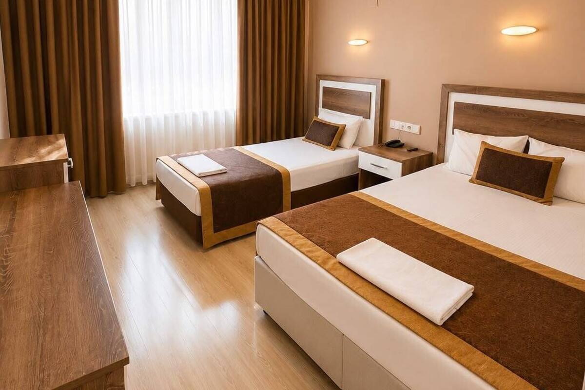 A hotel room with two beds, a desk, and a large window with curtains.