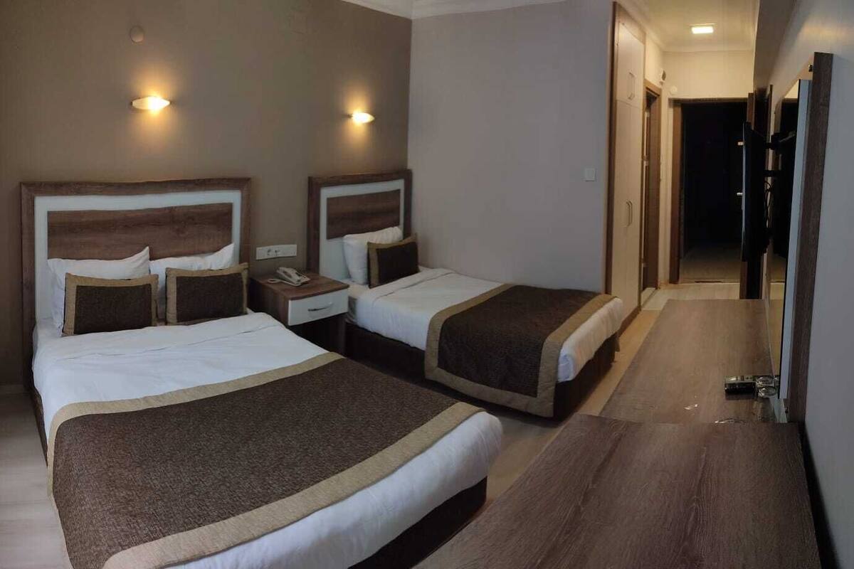 A hotel room with two beds, a nightstand, a telephone, and a hallway leading to a door.