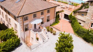 Un edificio grande con techo de tejas, piscina y una zona de estar al aire libre cubierta.