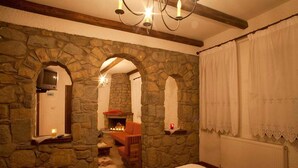 Um quarto acolhedor com paredes de pedra, lareira, cama e televisão.