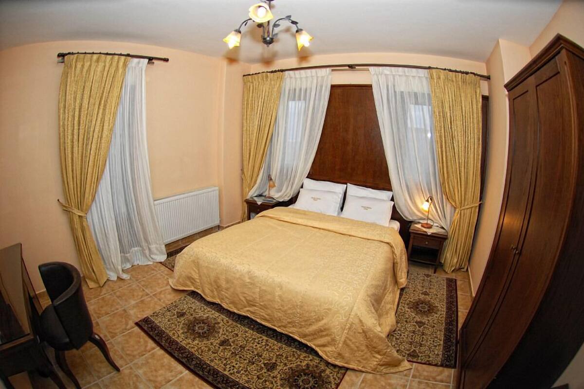 A bedroom with a bed, curtains, a nightstand, a chair, and a wooden wardrobe.