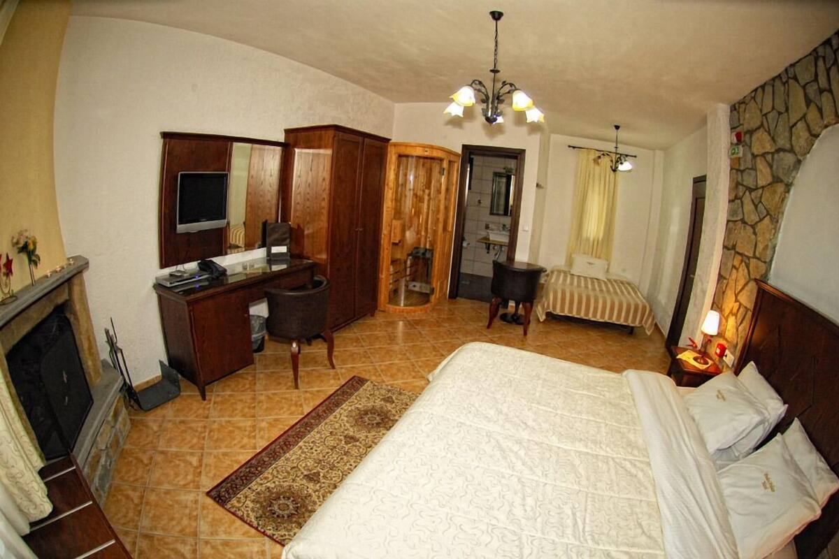 A bedroom with a bed, a desk, a television, a fireplace, and a stone wall.