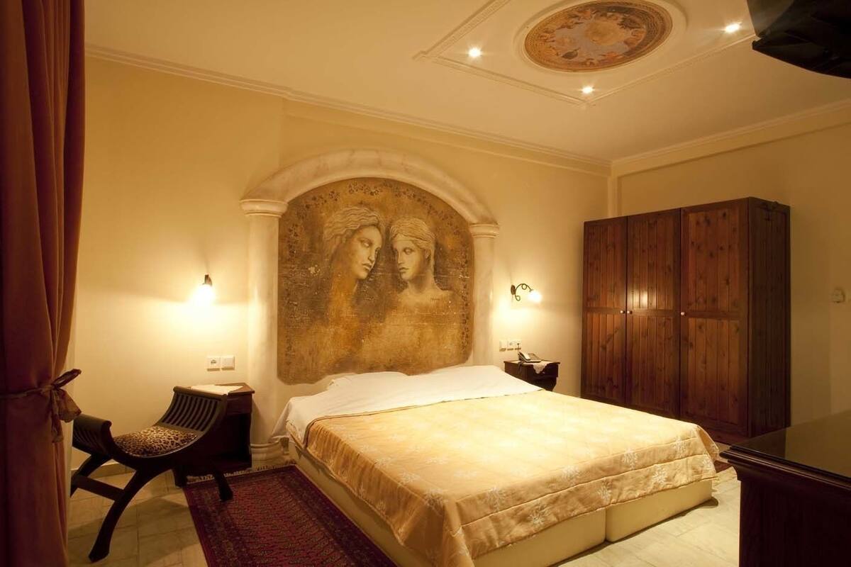 A bedroom with a bed, a wooden wardrobe, a nightstand, a lamp, and a chair.