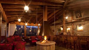 Uma área de estar acolhedora com lareira de pedra, vigas de madeira no teto e um bar com banquetas.