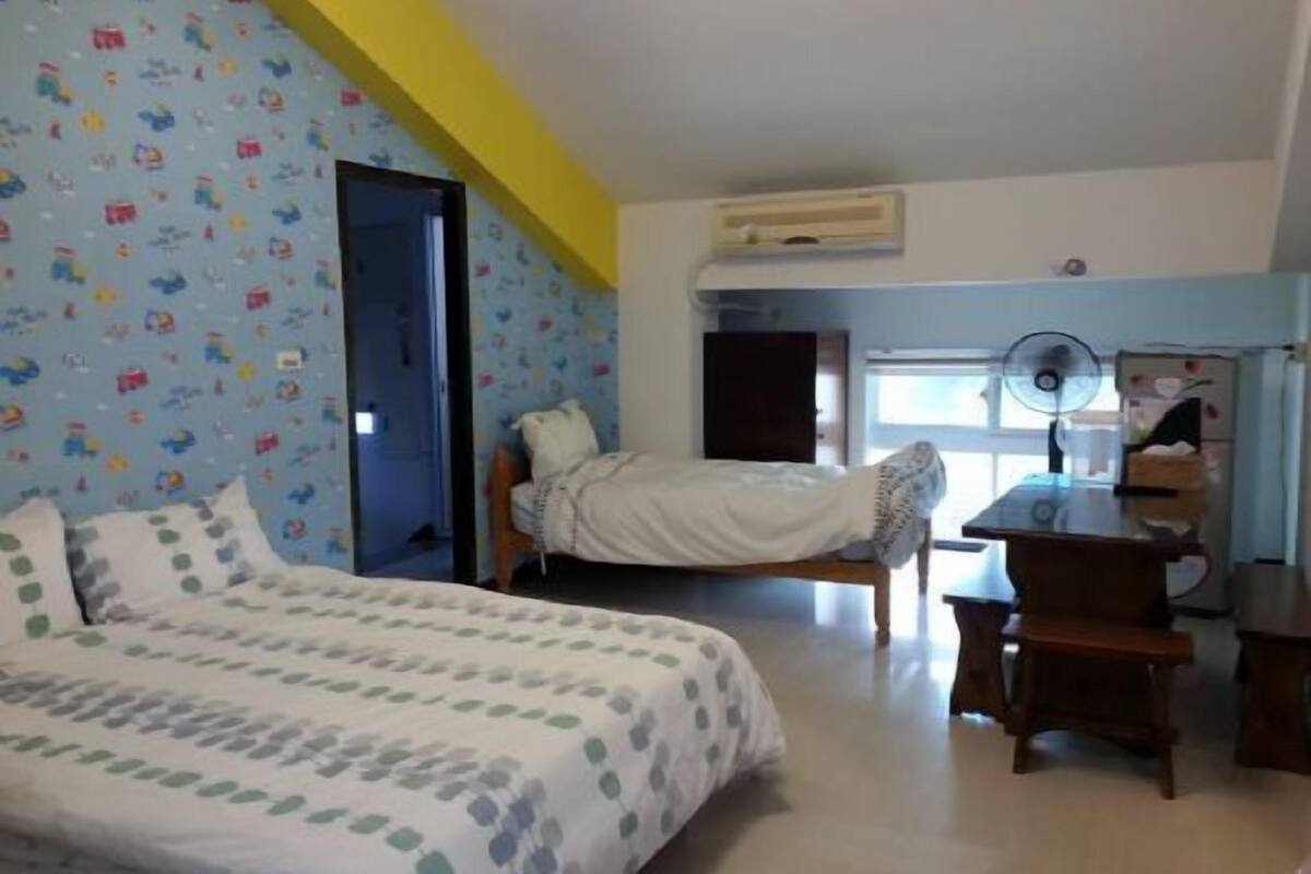 A bedroom with a bed, a desk, and a chair. There is a window with a view of the outside.