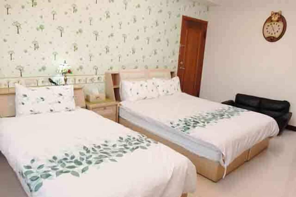 A hotel room with two beds, a wooden wardrobe, a nightstand, and a wall clock.