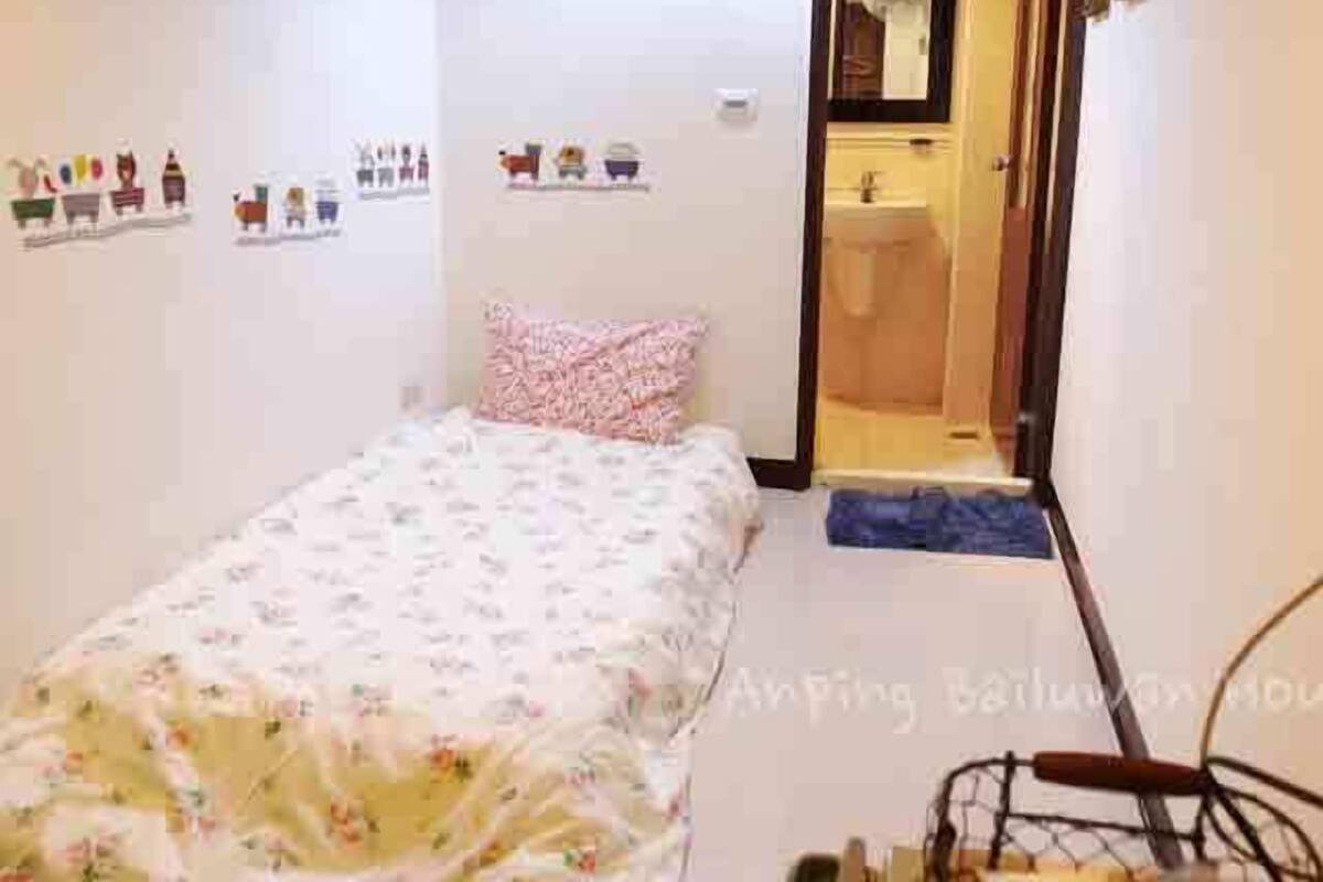 A small, neatly arranged bedroom with a single bed, a bedside table, and a mirror.