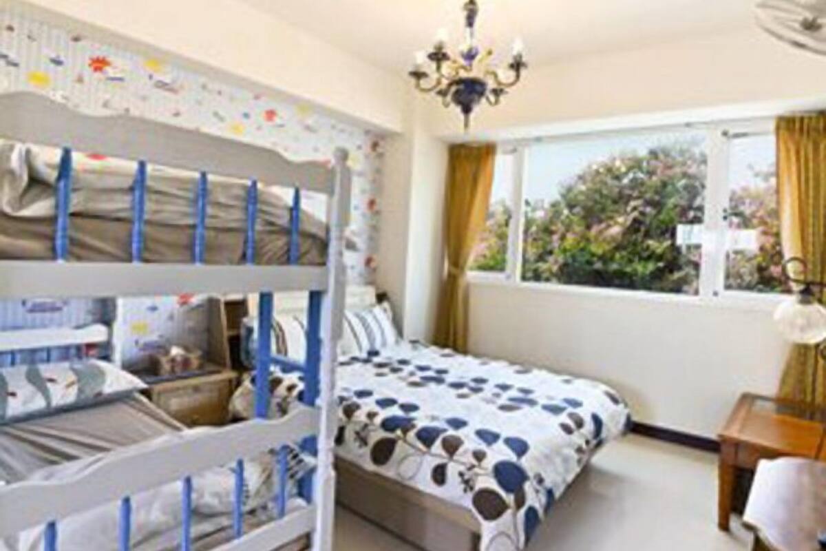 A room with bunk beds, a bed with a patterned bedspread, a window with curtains, and a chandelier.