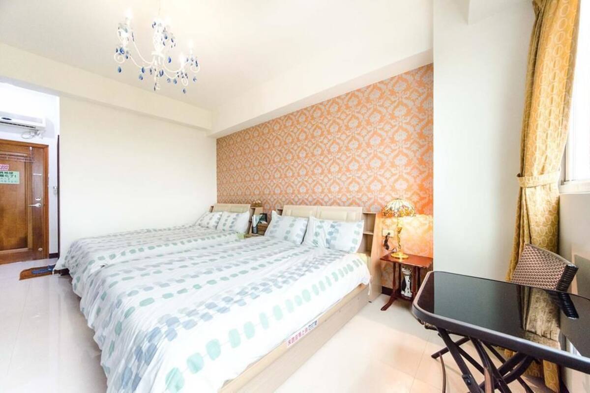 A bedroom with a bed, a nightstand, a table, and a chandelier.