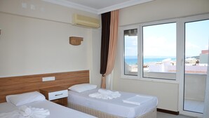 Une chambre d’hôtel avec deux lits, une tête de lit en bois, une table de chevet et une grande fenêtre donnant sur la mer et les bâtiments.