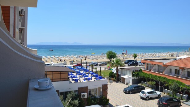 Un hôtel doté d’une terrasse donnant sur une plage, avec des chaises longues et une vue sur la mer.
