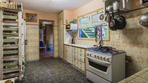 A compact kitchen with a gas stove, a microwave, and a sink. There is a small window with a view of a blue structure outside. - The Trip Hostel (Punta del Este)