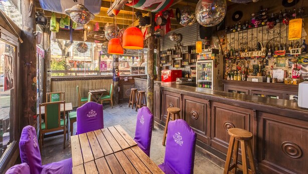 A bar with wooden furniture, a bar counter, and shelves with bottles. - The Trip Hostel (Punta del Este)