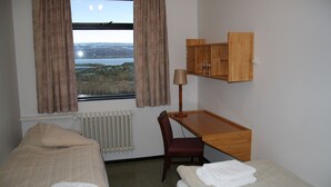 Ein Schlafzimmer mit zwei Betten, einem Holztisch, einem Stuhl, einer Lampe und Blick auf eine Landschaft durch ein Fenster.