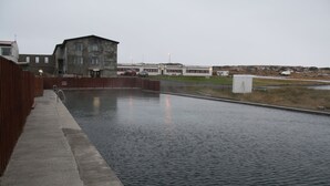 Ein Schwimmbecken mit Holzterrasse und einem Gebäude im Hintergrund.