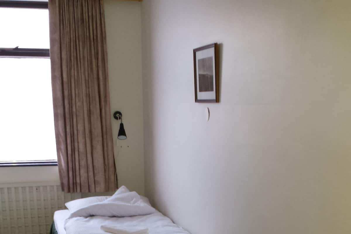 Una habitación con una cama, una silla, un radiador y una ventana con cortinas.