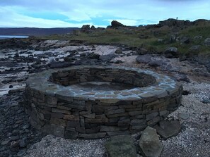 Une structure circulaire en pierre, qui pourrait être un puits ou un foyer, entourée d’un paysage rocheux à la végétation clairsemée.