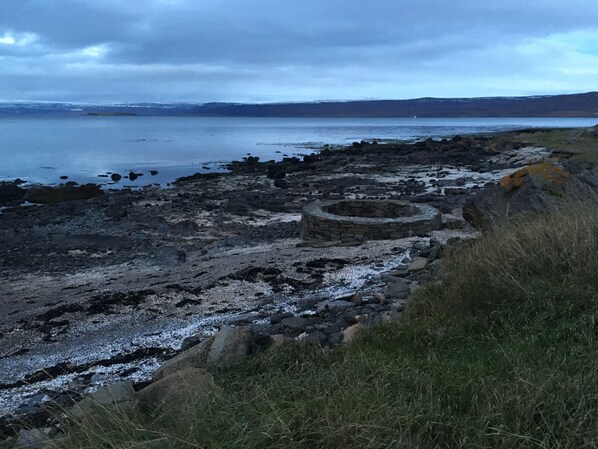 A rocky shoreline with a circular stone structure, possibly a well or a wellhead, surrounded by grass and rocks. - Hotel Reykjanes (Reykjanes)