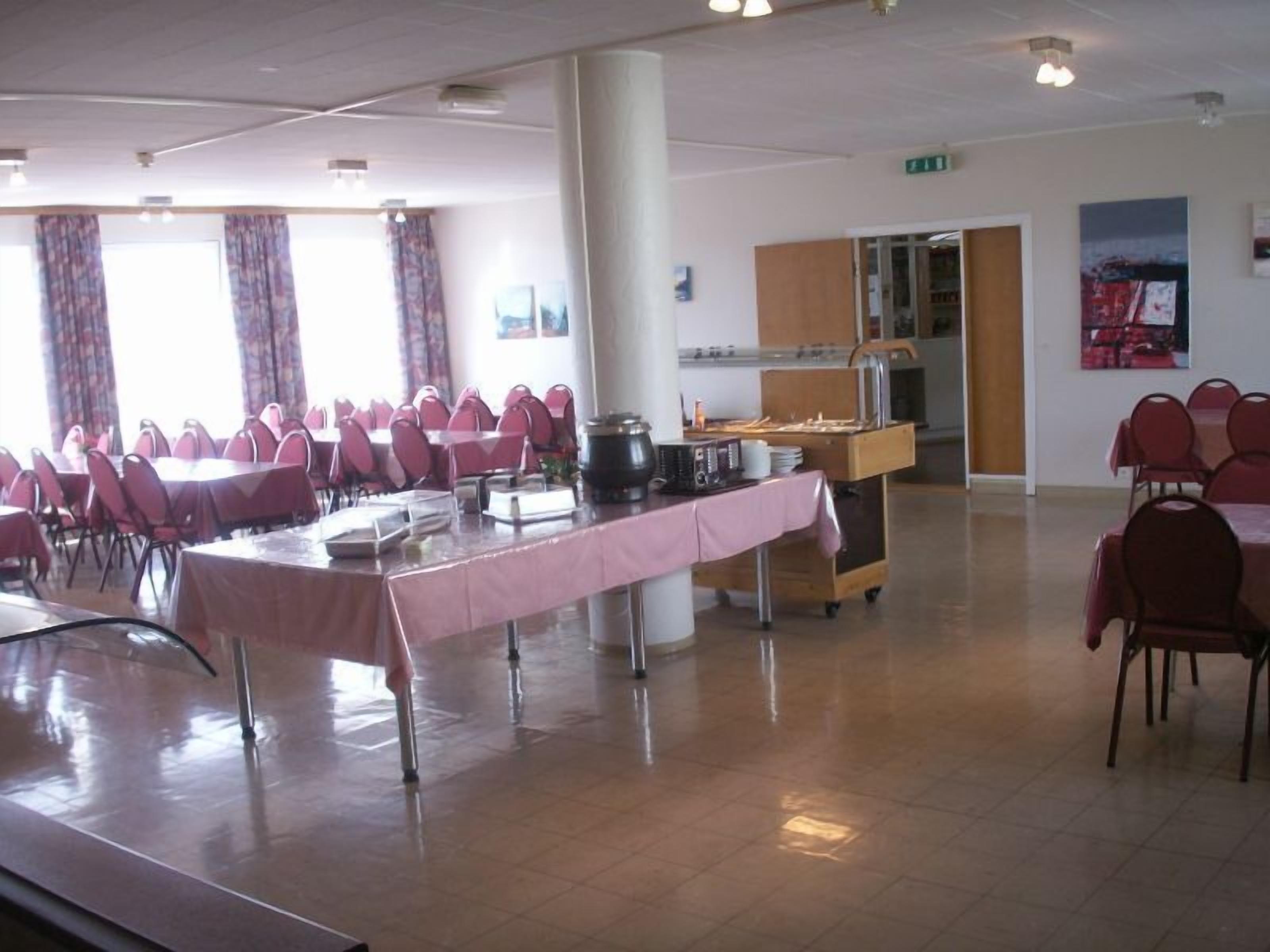 A spacious room with multiple tables and chairs, a kitchen area, and a large pillar.
