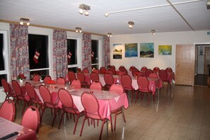 Une grande salle à manger avec de nombreuses tables rondes recouvertes de nappes roses et des chaises rouges.