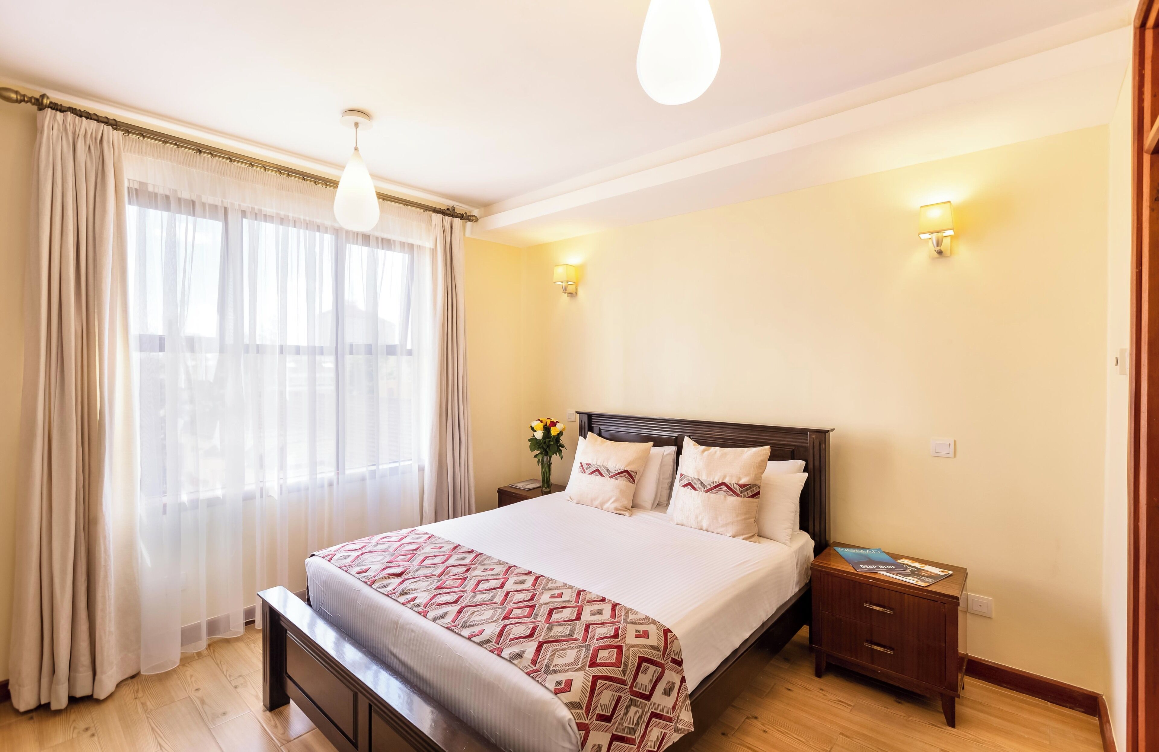 A bedroom with a bed, bedside tables, a bench, curtains, and a window.