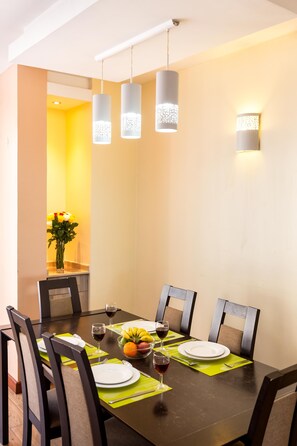 A dining area with a dark wooden table, green placemats, and chairs. There are two pendant lights above the table, and a wall-mounted light fixture to the right. - Fedha Residences (Nairobi)