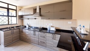 A modern kitchen with a black countertop, stainless steel appliances, and wooden cabinets. - Fedha Residences (Nairobi)