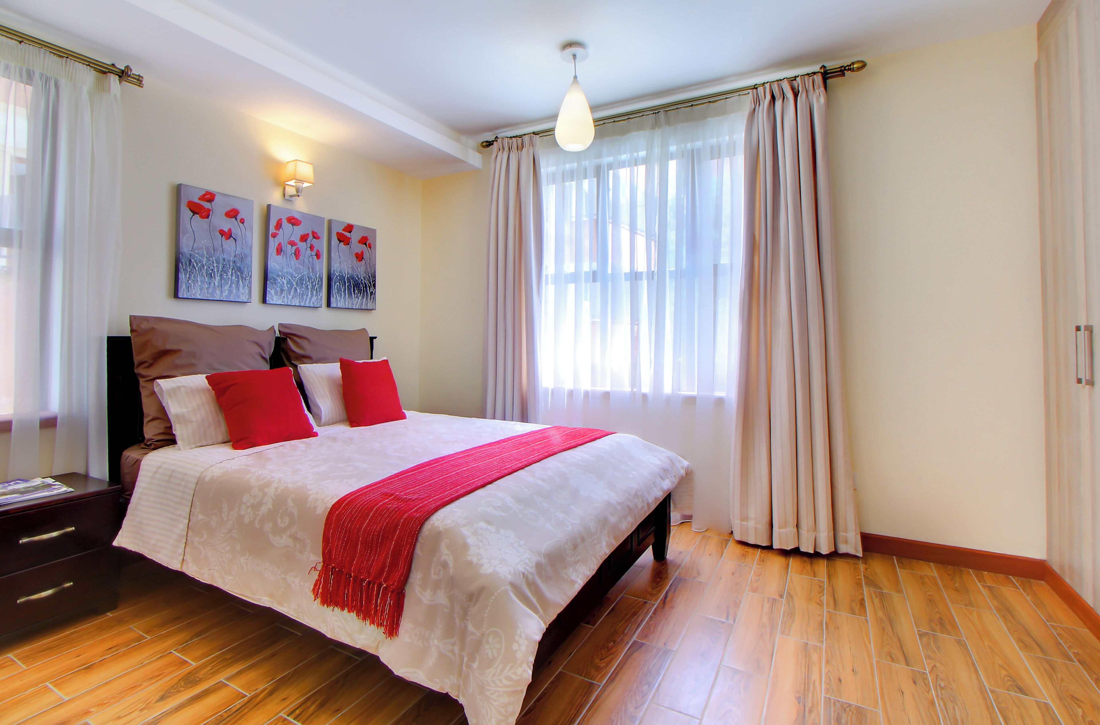 A bedroom with a large bed, a nightstand, a lamp, and a window with curtains.