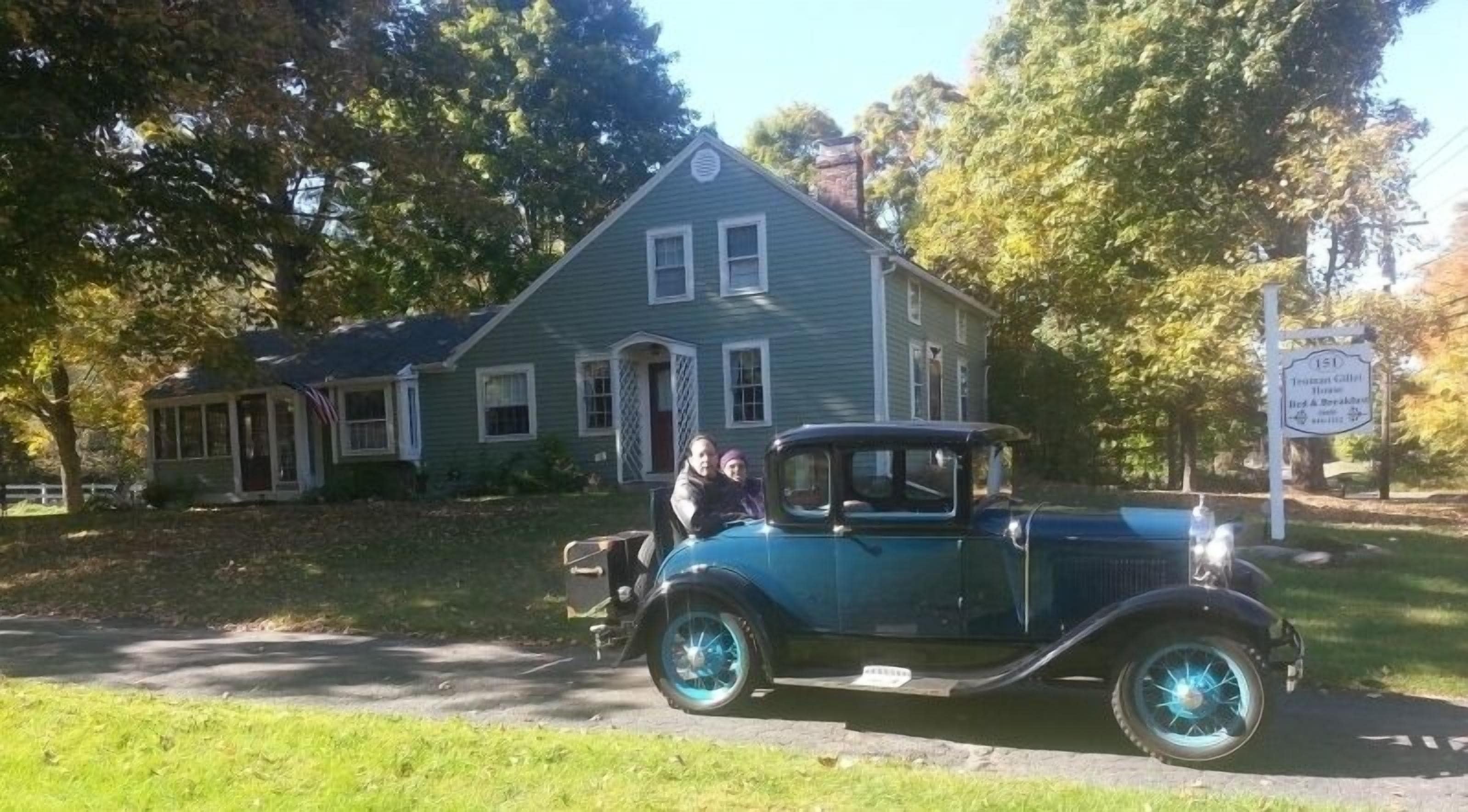 A vintage car parked in front of a house with a sign indicating it is a historic site.